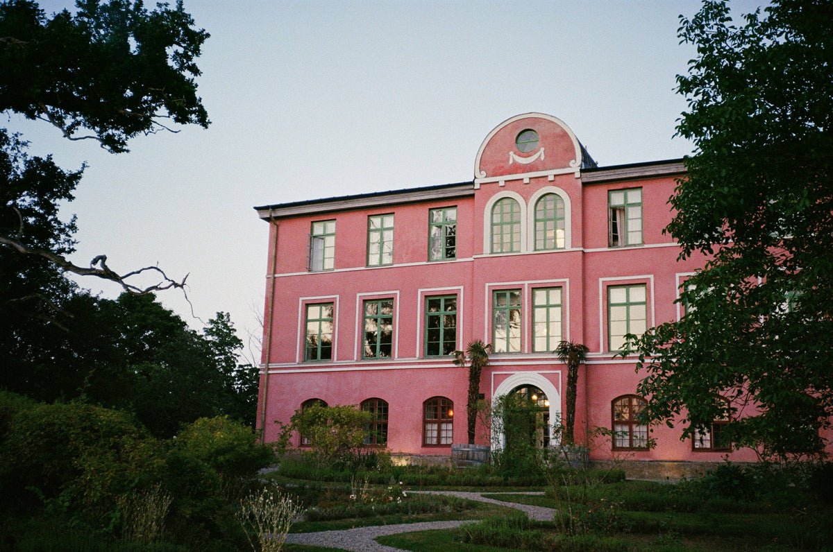 A pink manor house at dusk behind a summer garden in Blekinge
