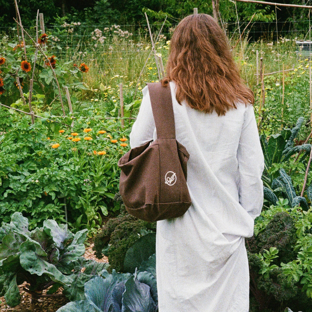 A woman in a garden with the dark brown Dreamer Extra Bag over her shoulder