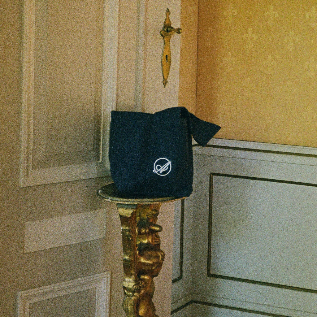 Shadow Extra Bag in navy with the embroidered Abelo emblem on a gilded pedestal
