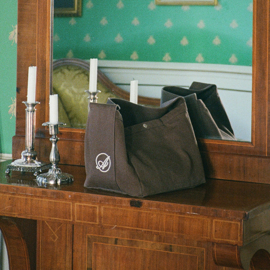 Dreamer Extra Bag in dark brown on a wooden dresser beside silver candlesticks