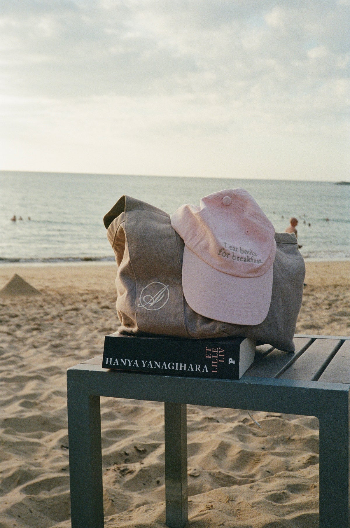 An Abelo bag and a pink Abelo cap resting on a book on a table by the sea