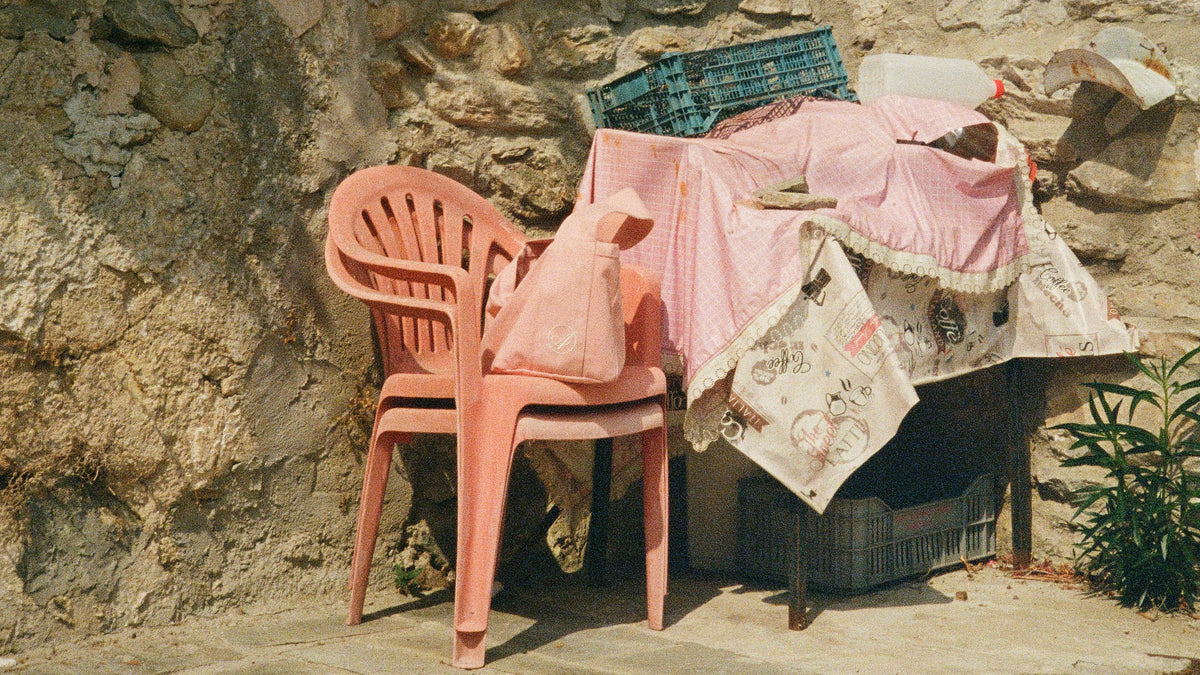 A pink plastic chair and a table draped in pink cloth against a rough stone wall