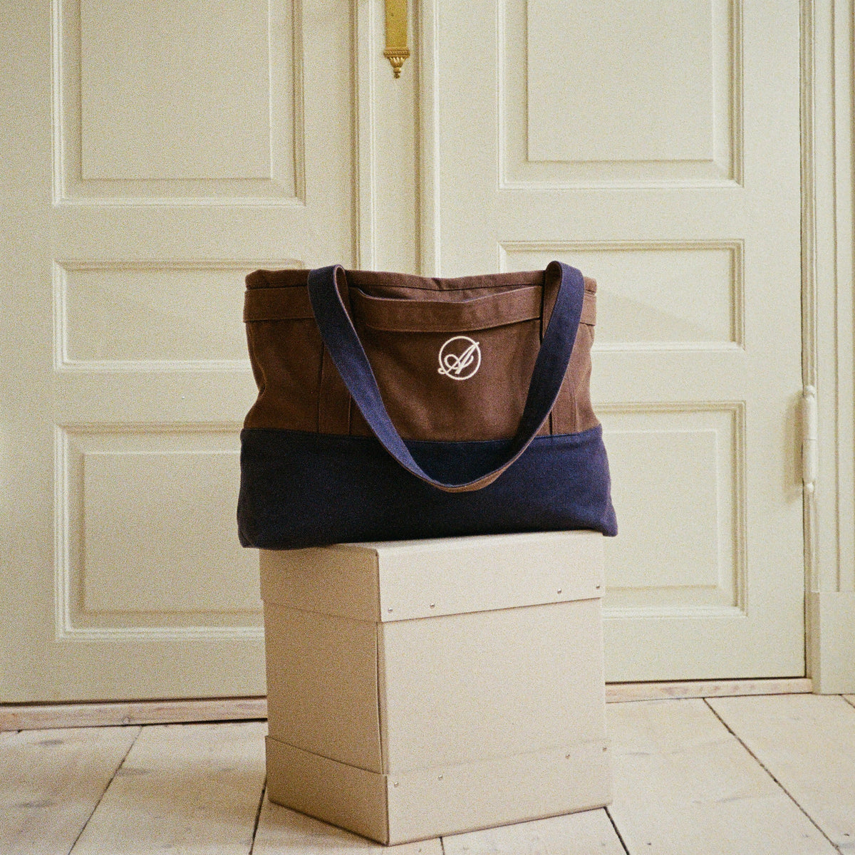 Ehrengard's Travel Bag in dark brown and navy on a pale box, front view with the embroidered Abelo emblem