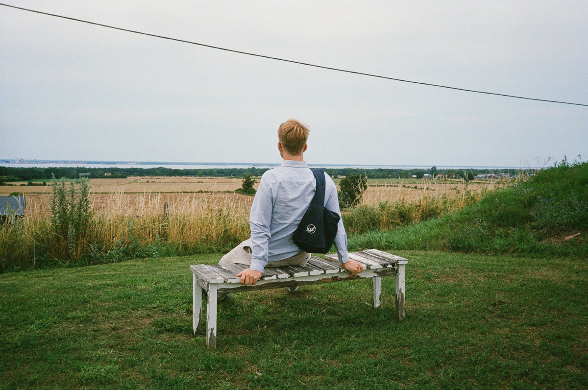 A man on a weathered bench looking out over fields towards the Baltic Sea