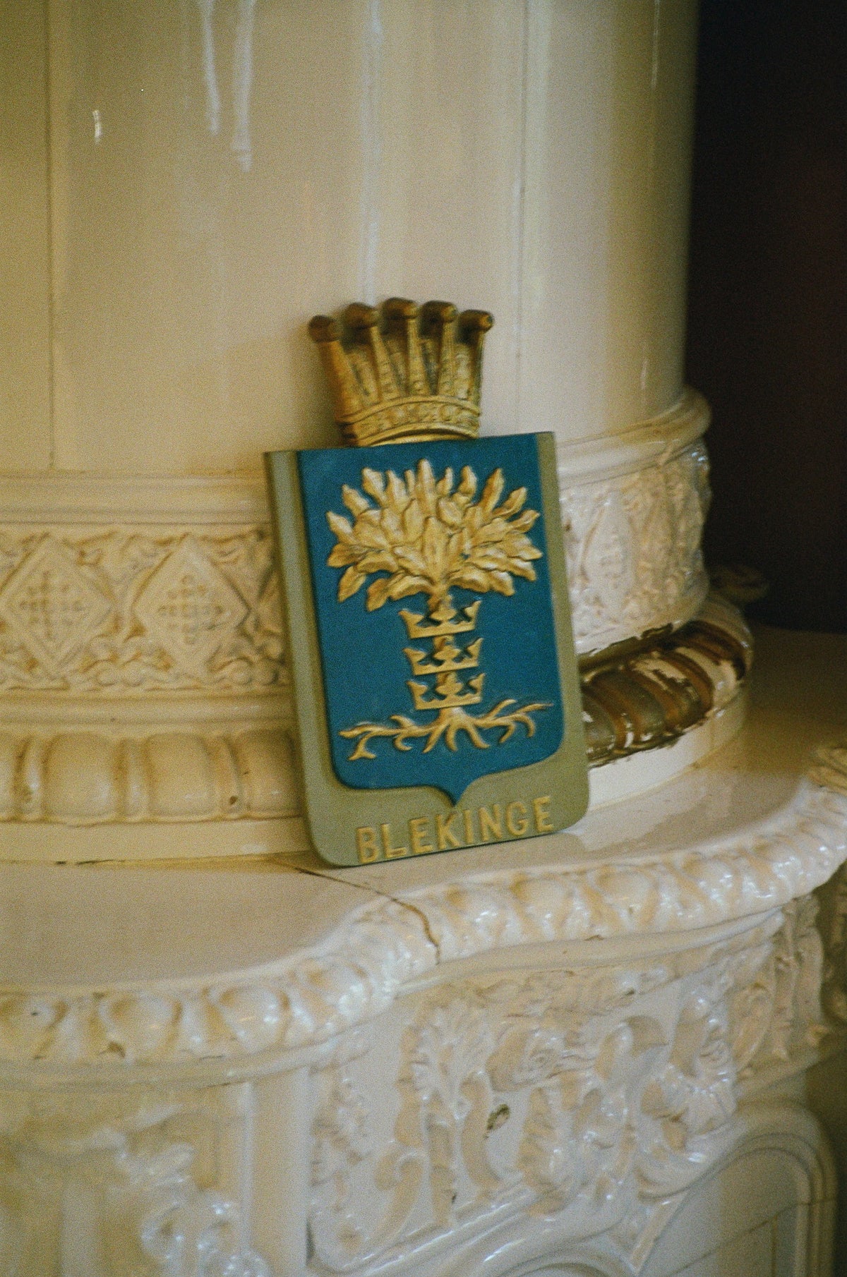 The Blekinge coat of arms, an oak tree above three crowns, resting on a white tiled stove