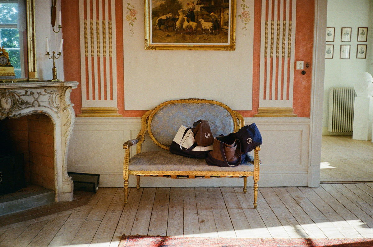Brown, cream and navy Abelo bags resting on a gilded sofa in a manor room with a marble fireplace